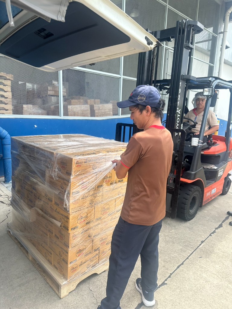 A team member wrapping a pallet of Khon Khu Krua cartons beside a forklift as it is loaded